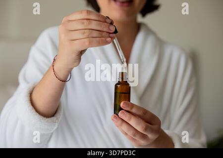 Amber glass dropper bottle resting on bathrobe while pipette drawing serum in spa Stock Photo