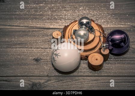 Purple, silver and white Christmas baubles arranged on rustic wooden slices over glitter wooden background, festive still life with copy space. Stock Photo