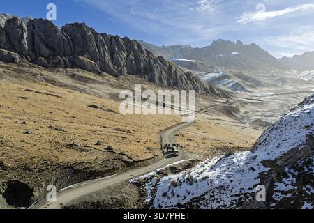 Aerial view of a winding road cutting through the rugged terrain with snow-dusted peaks under a bright sky, Yushu, Qinghai, China. Stock Photo