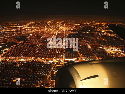 Flying over the night city by plane. The view from the window of a passenger plane during the flight, the wing of the turbine engine of the aircraft Stock Photo