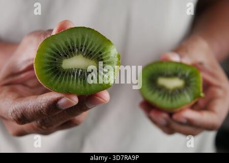 Freshly cut kiwi halves held in hands for display Stock Photo