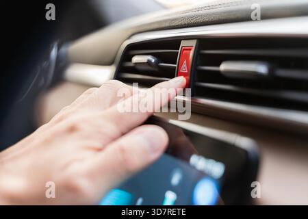 Close-up of a hand pressing the red hazard warning button on a modern car dashboard, highlighting emergency alert control, safety awareness, and vehic Stock Photo