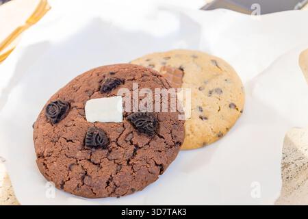 Two large soft cookies with chocolate chips on white paper close-up. Stock Photo