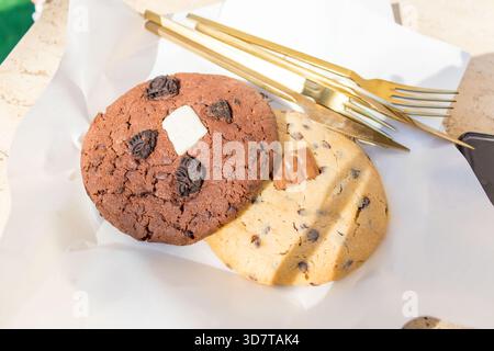 Two large soft cookies with chocolate chips on white paper close-up. Stock Photo