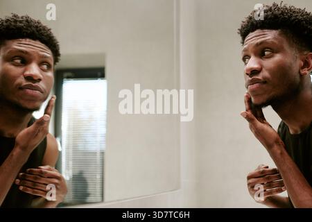 Young Adult Black Man Touching Face While Looking at Reflection in Mirror Stock Photo