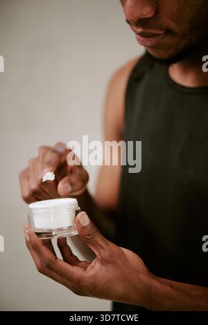 Young Adult Black Man Applying Moisturizer Cream during Morning Skincare Routine Stock Photo