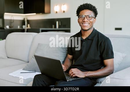 Portrait of Young Adult Black Man Smiling While Using Laptop in Morning Stock Photo