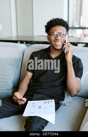 Young Adult Black Man Smiling While Talking on Smartphone in Morning Light Stock Photo
