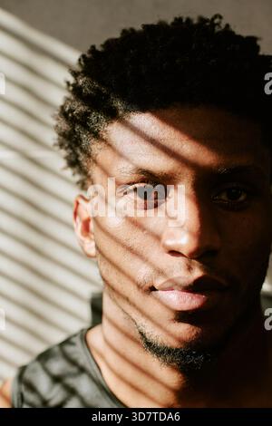 Portrait of Young Adult Black Man Enjoying Morning Sunlight Indoors Stock Photo