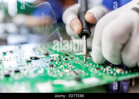 Closeup of worker in protective gloves soldering electronic circuit board with hot iron and visible smoke during assembly process Stock Photo