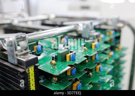 Close view of assembled green printed circuit boards stacked in rack inside modern automated electronics manufacturing plant Stock Photo