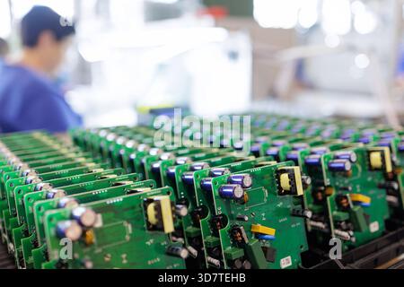 Rows of assembled green printed circuit boards in racks with factory worker in background at modern electronics production line Stock Photo