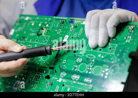 Close up of technician holding green PCB and soldering connections by hand in electronics factory, illustrating precision repair and quality control Stock Photo