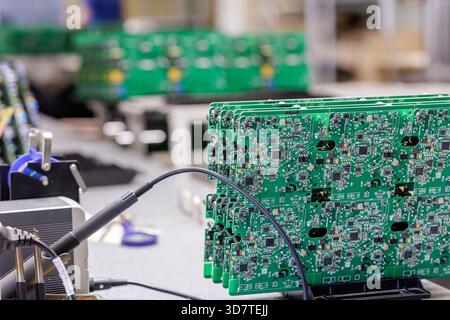 Stack of green printed circuit boards connected to test equipment at electronics factory workstation focused on quality control and diagnostics Stock Photo