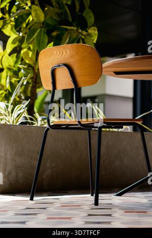 Outdoor comfort. A comfortable chair placed on a decorative tile floor next to a concrete planter with vibrant green foliage. Stock Photo