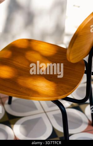Pattern and texture contrast. High-angle view emphasizes the warm wood grain of a chair seat and the cool, intricate design of the floor tiles. Stock Photo