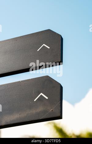 Pointing the way. Simple, minimalist design of two dark signs featuring prominent white arrows pointing upwards, set against a clear blue sky, represe Stock Photo