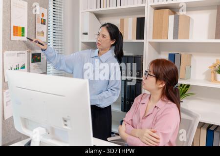 Two Asian office colleagues working together in the same department, reviewing documents and discussing project details during a team meeting, showing Stock Photo