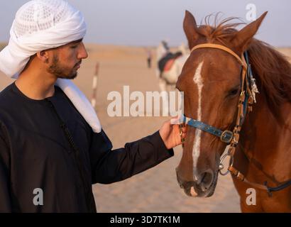 Arab man wearing traditional clothing petting a horse in the middle of the desert. High quality photo Stock Photo