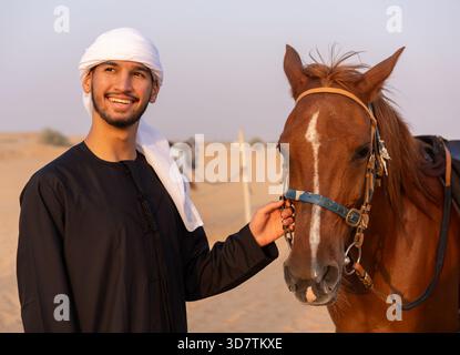 Arab man wearing traditional clothing petting a horse in the middle of the desert. High quality photo Stock Photo