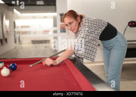 Woman taking a precision shot on a red pool table during a game Stock Photo