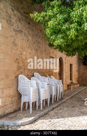 Plastic chairs stacked by old stone wall in Sencelles, market day, Mallorca Stock Photo