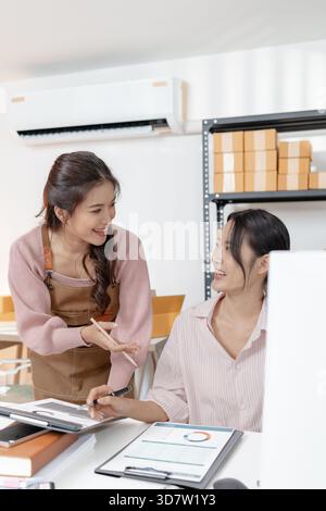 Two young women working together in a small office, discussing documents and reviewing business data. Their teamwork highlights collaboration, plannin Stock Photo