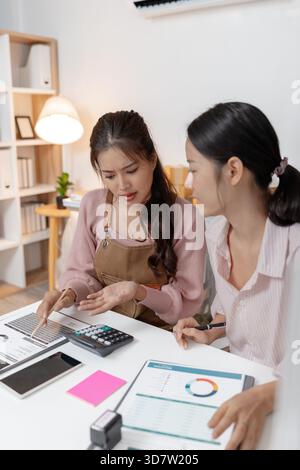 Two young women working together in a small office, discussing documents and reviewing business data. Their teamwork highlights collaboration, plannin Stock Photo