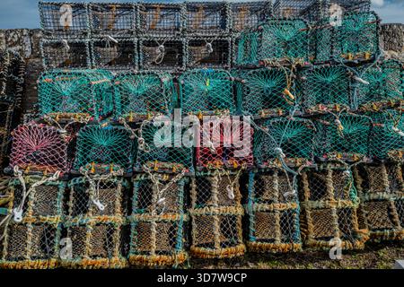 Stacked multicolored lobster traps with nets piled against a stone wall. Keiss harbour, Scotland Stock Photo