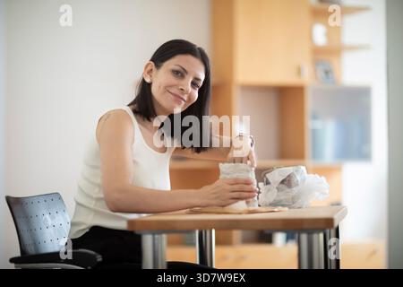 Woman sculpting clay at a table in a bright room, focused on her craft. Germany Stock Photo