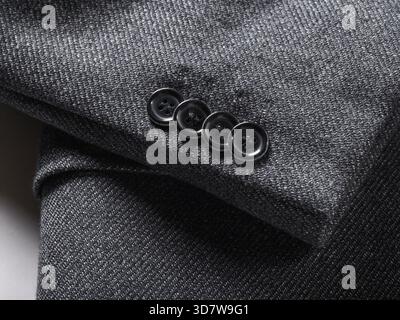 Close-up of a dark grey wool suit sleeve with four black buttons stitched on. Stock Photo