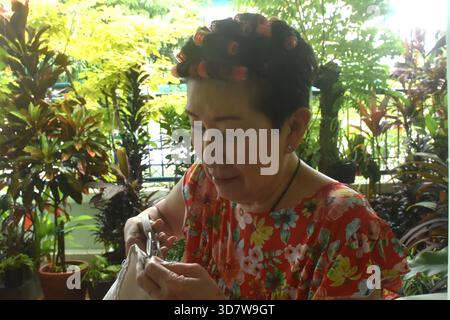 Asain elder woman sewing cloth for repairing in home front yard Stock Photo