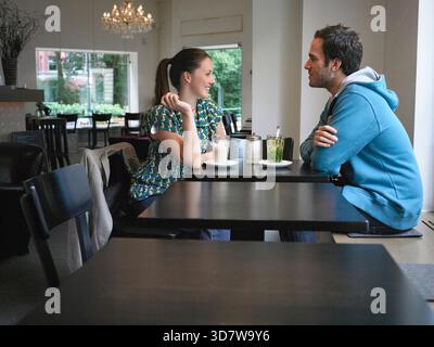 A couple enjoys a conversation over drinks in a cozy, modern cafe interior. Germany Stock Photo