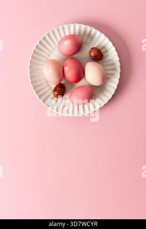 A collection of beautifully dyed Easter eggs in various shades rests on a decorative plate, set against a soft pink background, celebrating the joyful Stock Photo