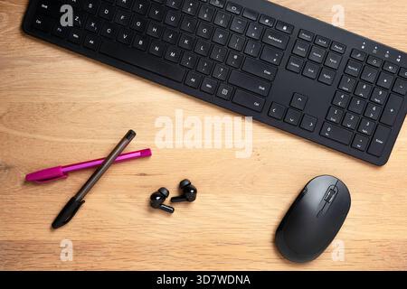 Organised desk workspace with keyboard, mouse, pens, earbuds Stock Photo