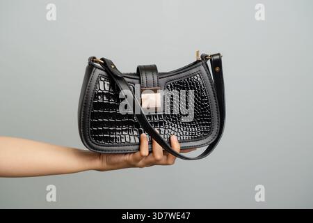 Black Patent Croc Embossed Shoulder Bag Held By Hand On Plain Background Stock Photo