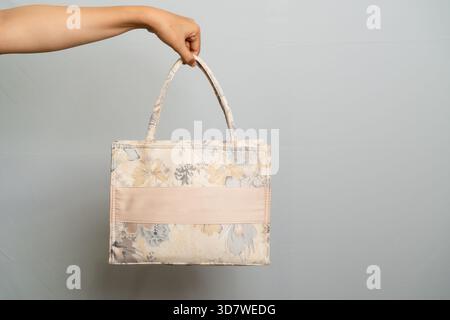 Hand Holding Embroidered Tote Bag with Floral Pattern and Satin Ribbon Detail Isolated on Gray Stock Photo