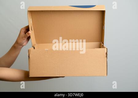 Hands Holding Open A Cardboard Box With Blue Accents On A Light Gray Background Stock Photo