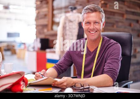 Fashion designer, mature man and notebook in workshop for sketching, design process and planning. Clothing production, startup owner or portrait in Stock Photo