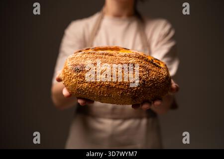 A baker holds out a large crusty seeded loaf, highlighting its texture, sesame seeds and handcrafted artisan quality Stock Photo