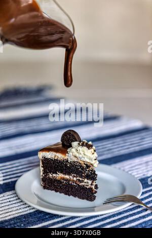 pouring chocolate sauce on a slice of chocolate chip cake with biscuit and cream Stock Photo