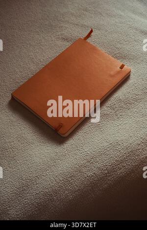 Orange leather notebook mockup on white textured surface. Stock Photo