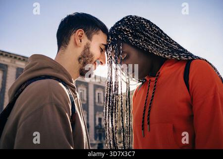 Young interracial couple sharing an intimate emotional moment outdoors in natural sunlight. Authentic expression of connection, support and vulnerabil Stock Photo