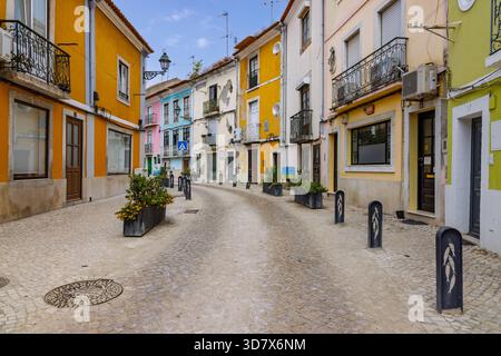 Picturesque curving cobblestone street in Setubal, Portugal. Brightly colored traditional houses, balconies, and planters line the charming alley. Stock Photo