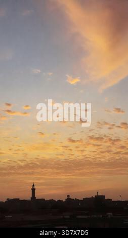 Beautiful sunset with a large building in the background. The sky is filled with clouds and the sun is setting Stock Photo
