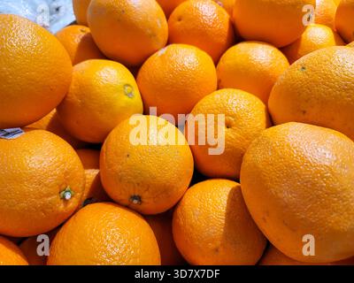 A bunch of oranges are piled up. They are all the same size and color. The oranges are sitting on a table Stock Photo