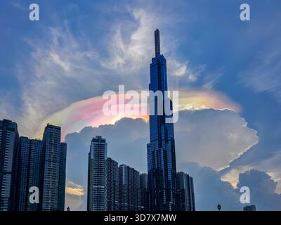 A rainbow is seen above a tall building. The building is in a city. The sky is cloudy Stock Photo