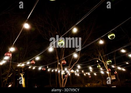 A string of Christmas lights with green and red balls hanging from the wires. The lights are lit up and the balls are glowing Stock Photo