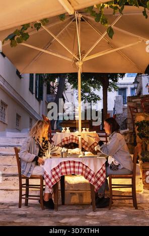 Two women friends sitting outdoors at a restaurant in the evening eating and drinking; Plaka, Athens, Greece, Europe Stock Photo