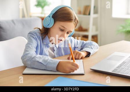 Teen boy, school pupil wearing wireless headphones studying online alone from home making notes Stock Photo